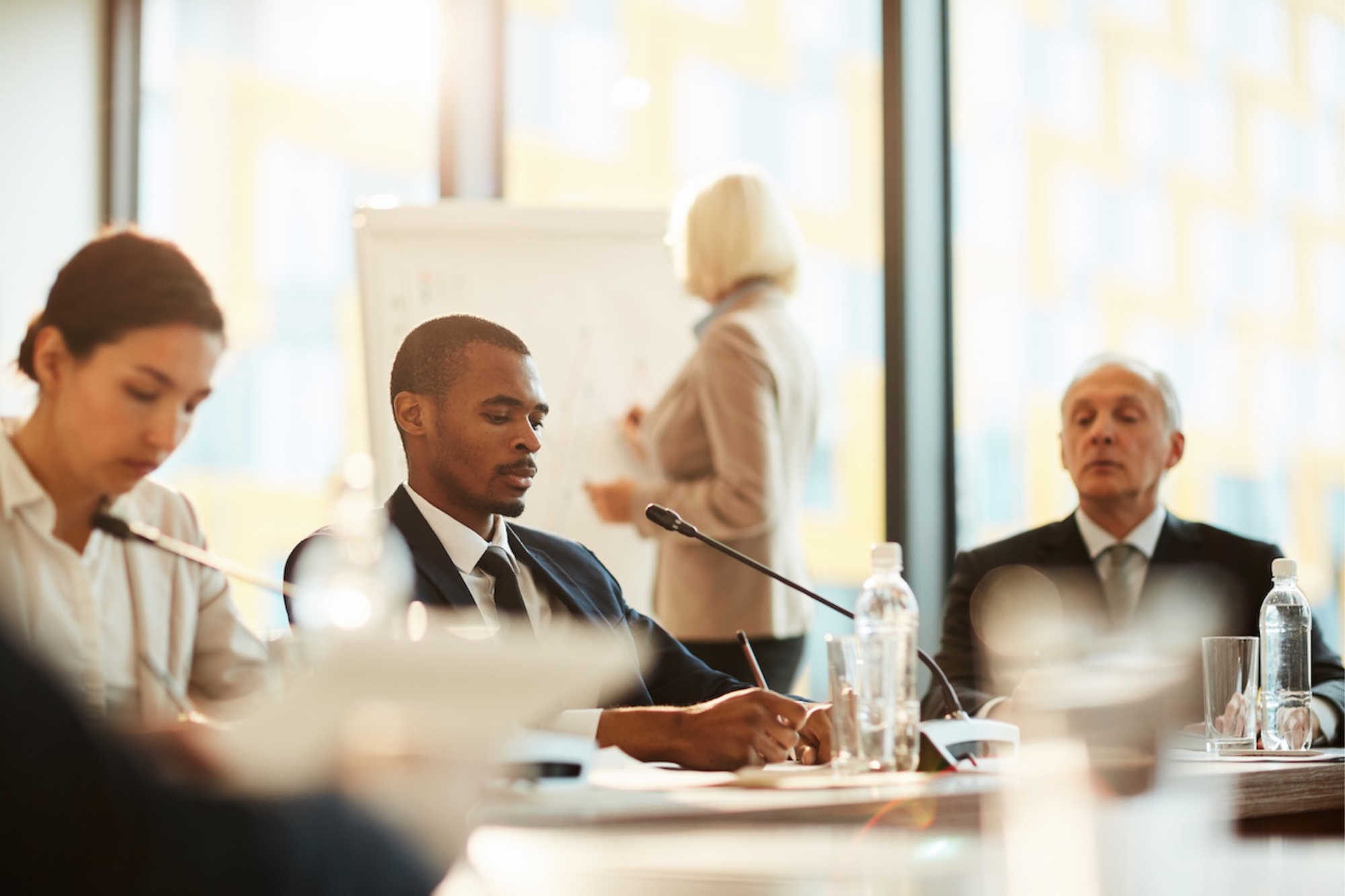 Executive team in a corporate boardroom meeting, professionals reviewing strategy while a presenter outlines plans on a whiteboard