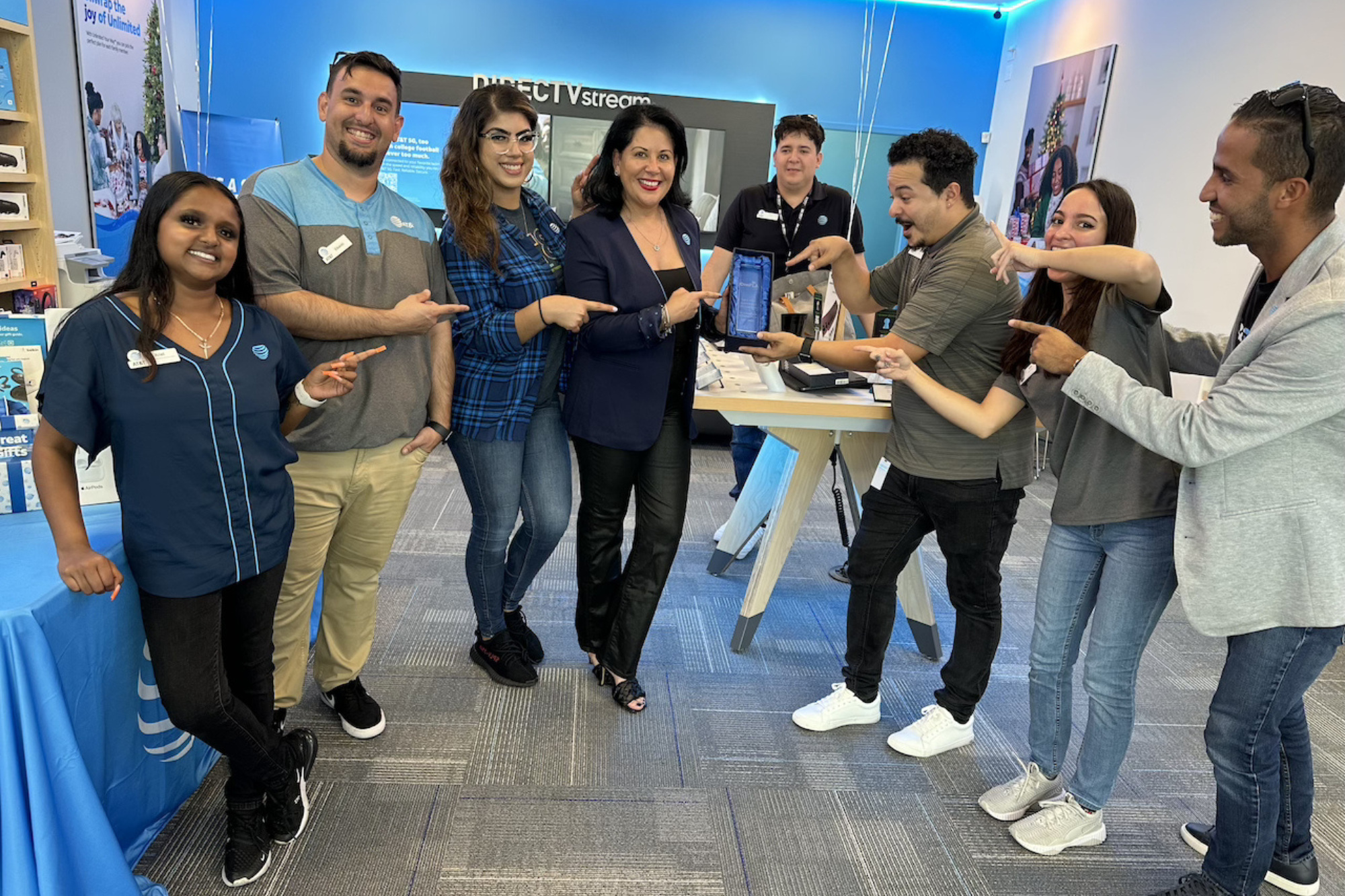 Retail team members inside an AT&T store smiling and pointing at a colleague holding an award or device during a team celebration.