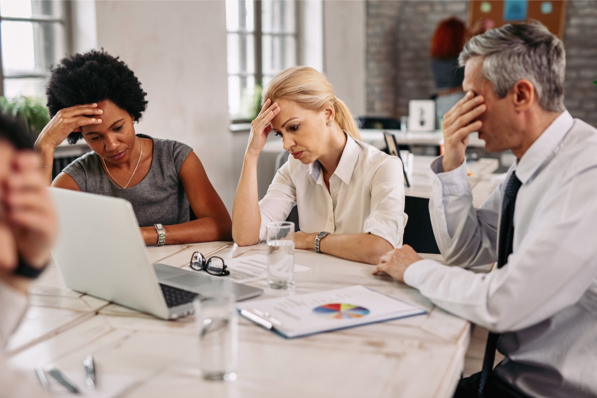 Stressed business team reviewing reports at a meeting table, professionals analyzing challenges and financial performance on a laptop