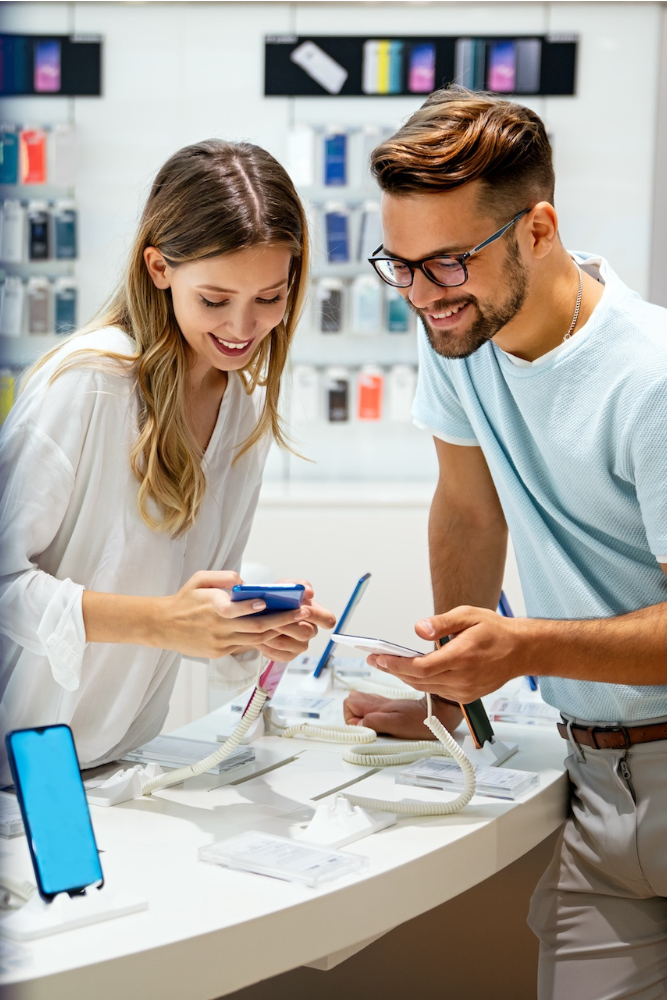 Customers in a mobile phone store comparing smartphones while exploring device features with assistance nearby